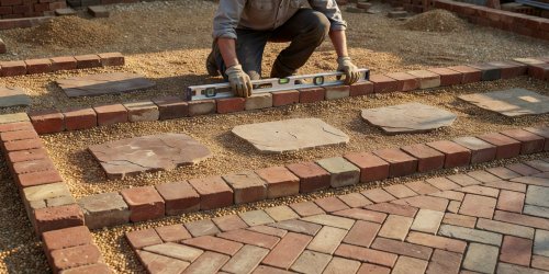 Person setting a spirit level across clay brick edging enclosing compacted golden gravel and sandstone step pads